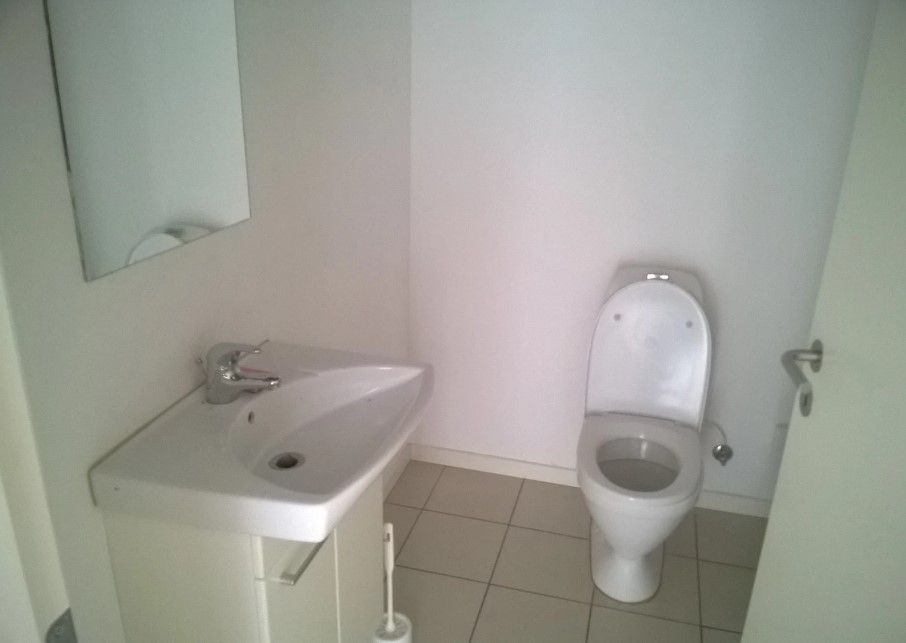 En moderne hvid badeværelse med en stor spejl og en toilet med hvidt toiletpapire. Et hvidt vask med en børste og en