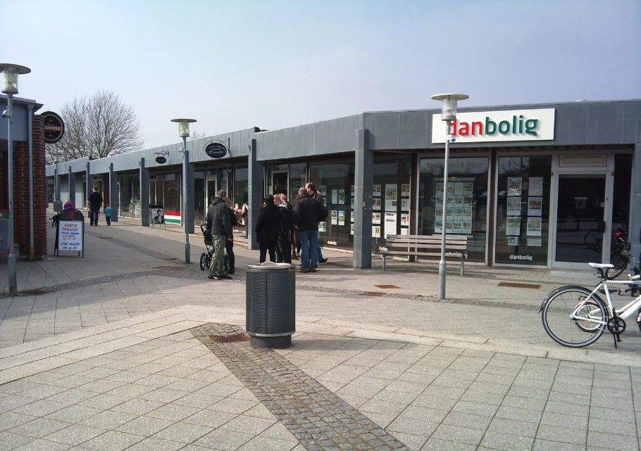 Folk samles udenfor butikken Danbologi. En person står ved en cykel, og en anden læner mod en vogn. Der er to bænke og to