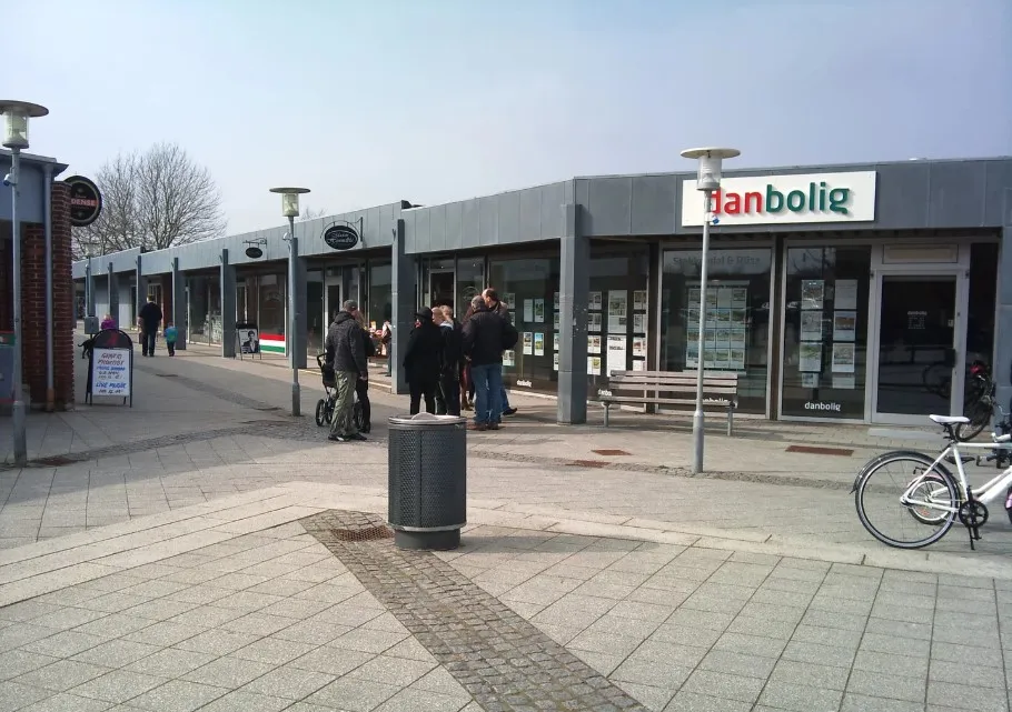 Folk samles udenfor butikken Danbologi. En person står ved en cykel, og en anden læner mod en vogn. Der er to bænke og to