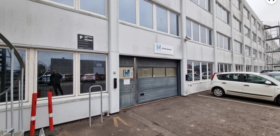 På fabriksområdet i Ballerup er der et lager med kontor og garage til leje. En hvid bil parkeret udenfor