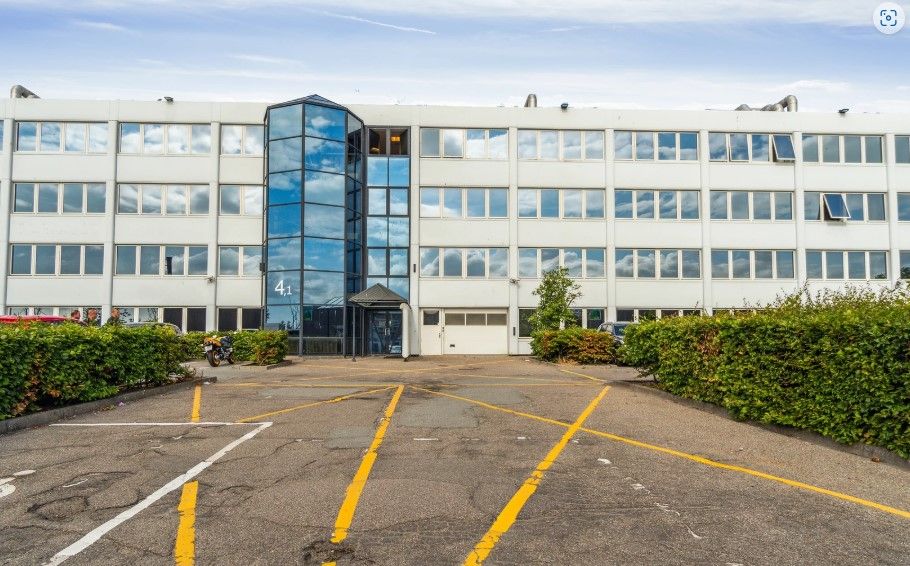 Parkeringsplads med gult linjeforløb uden for et kontorbygning i Ballerup