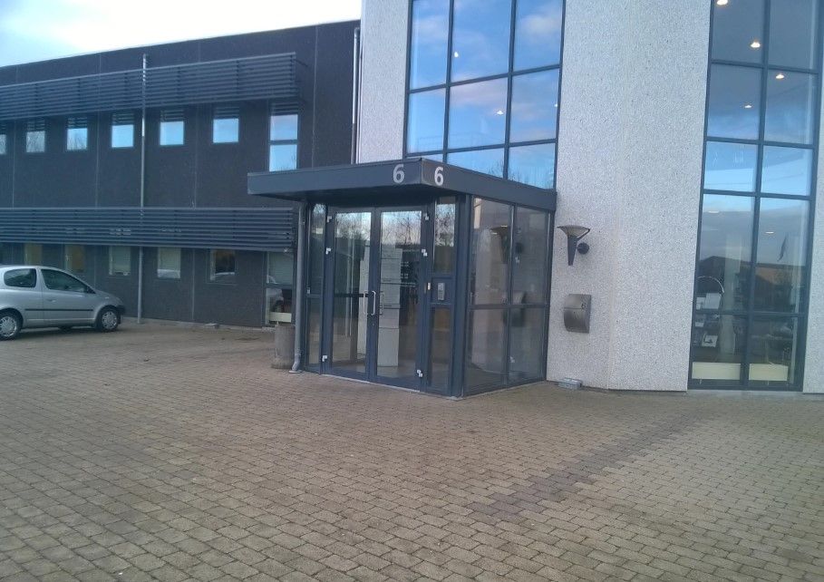 Kontorbyggeri med glasvinduer og moderne design, nummer 6. En dør med glas og metal, og en bil parkeret.