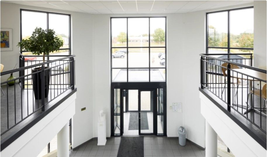 Indgangsparti til kontorlokaler i bygningen med dobbelt glasdør og balkoner med træborde og stole samt en plante