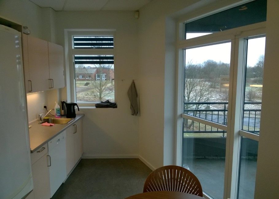 En lille køkken med et køleskab, en stol, et bord, en spidset lysestage og en glasdør med udsigt til en snepark