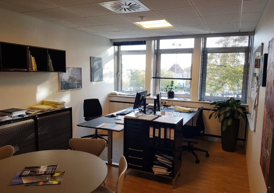Kontorlokale med skrivebord, stol, monitor, plante, kabinet, hylde, og vinduer med gardiner i Vejle