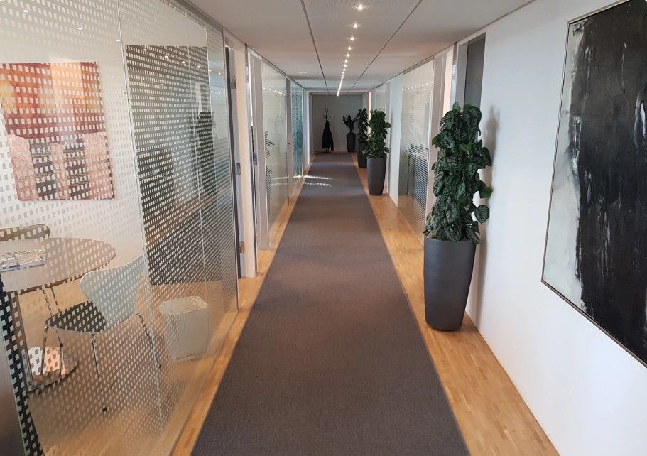 En lang og bred gang i et kontorlokale med høje glasvægge og en brun gulvbelægning