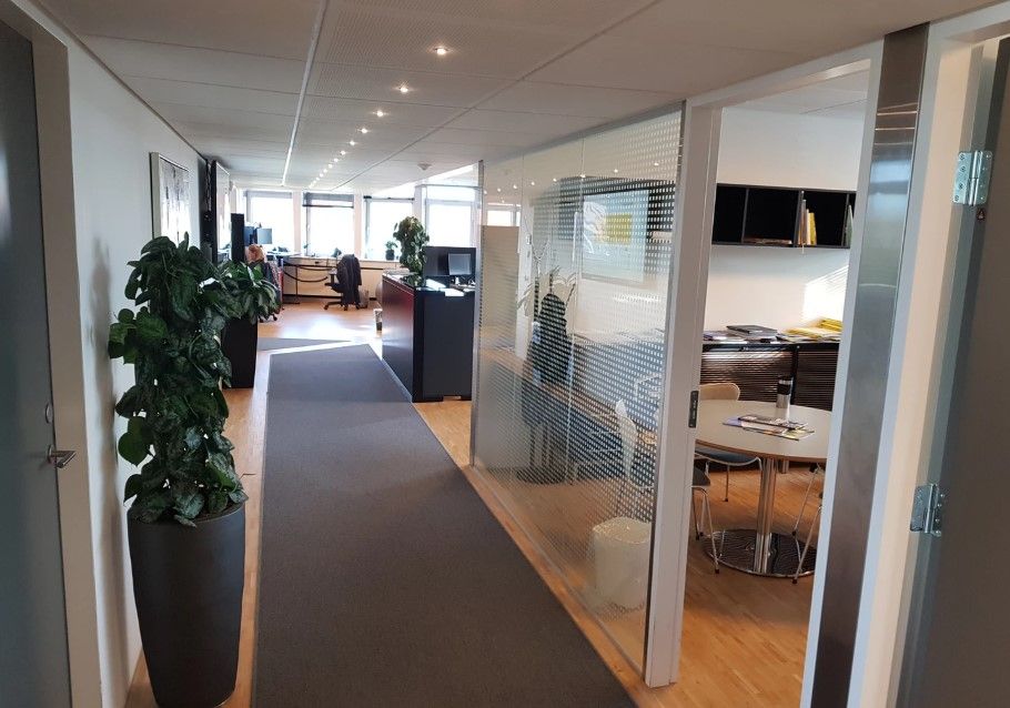 Kontorlokale med moderne møbler, to stolpeplanter, runde borde og høje lofter med indbyggede lygter