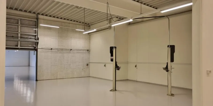 Foto af et tomt lokale med hvide vægge, højloft og store garagedøre samt to store gulvmonterede støttebøjler