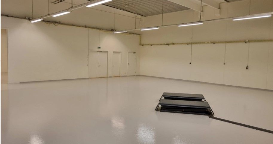 Store tomme lokaler med hvide vægge og gulv samt to døre og hængende rørledninger og lys.