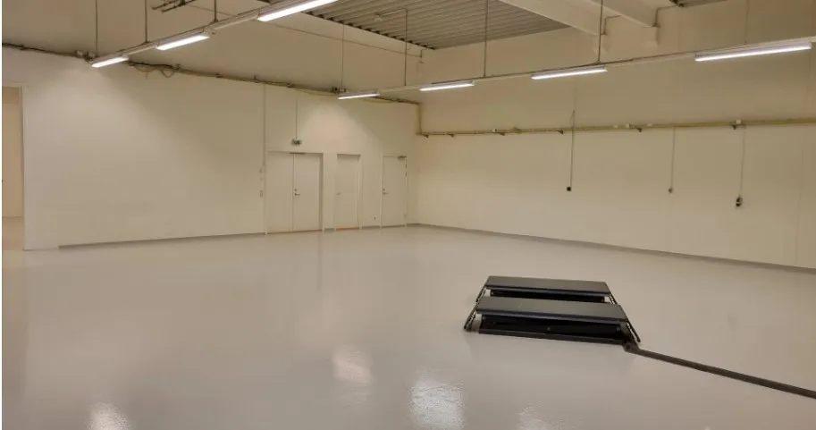 Store tomme lokaler med hvide vægge og gulv samt to døre og hængende rørledninger og lys.