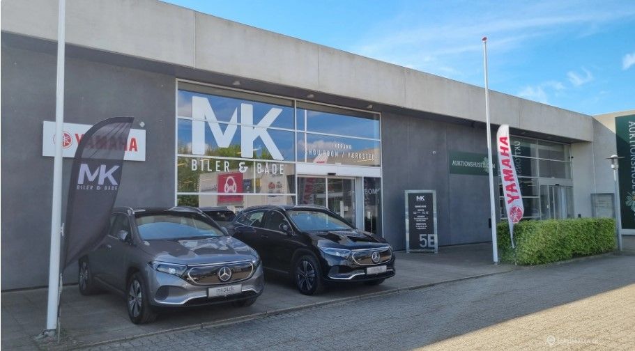 To biler parkeret udenfor en bilforretning. En Mercedes og en anden bil parkeret udenfor. Forretningen hedder MK og har et