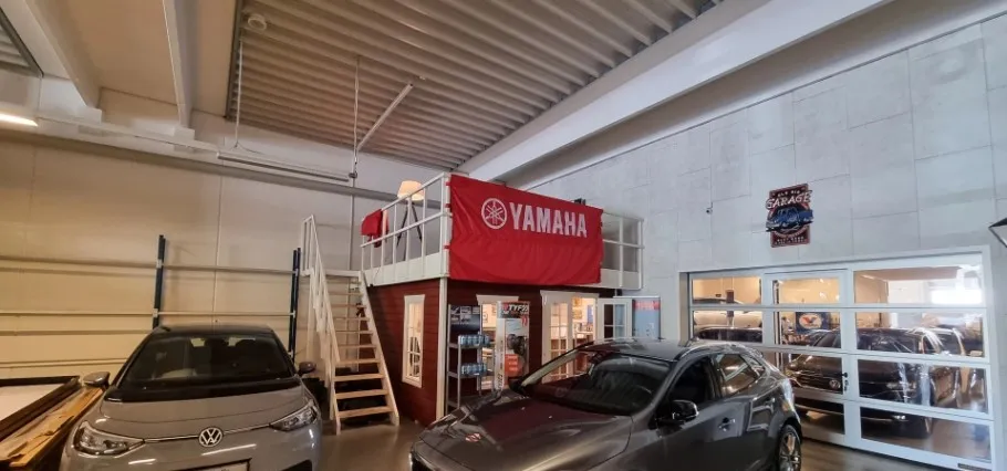 Garage med biler og loftsværelse med Yamaha-banner og trappe til loftsværelset
