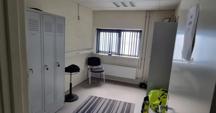 En lille stue med to hvide garderobeskabe, en stol, en stol med en sort hat, en radiator og en åben dør med en gul og sort