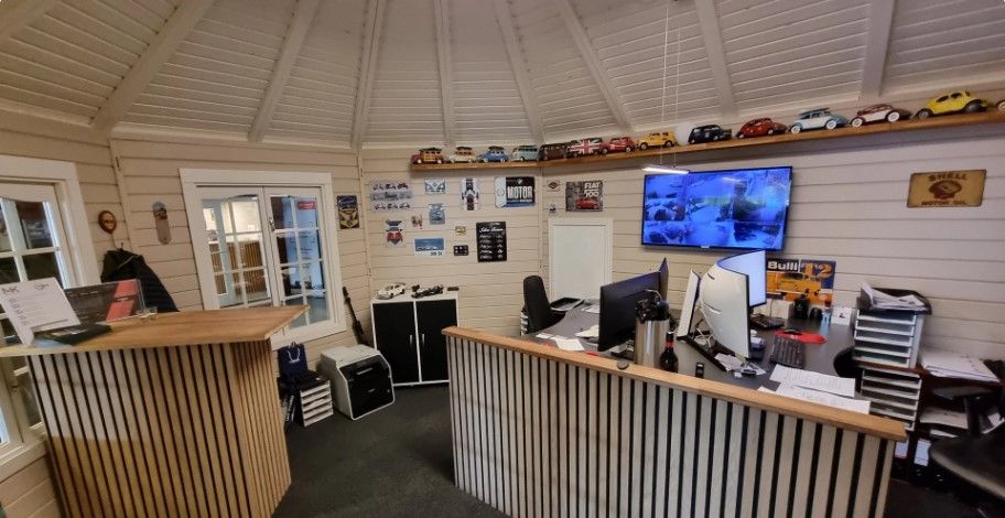 Køkken med skrift på væggen, monitorer og skærme, samt en række bilmodeller og andre genstande på hylden