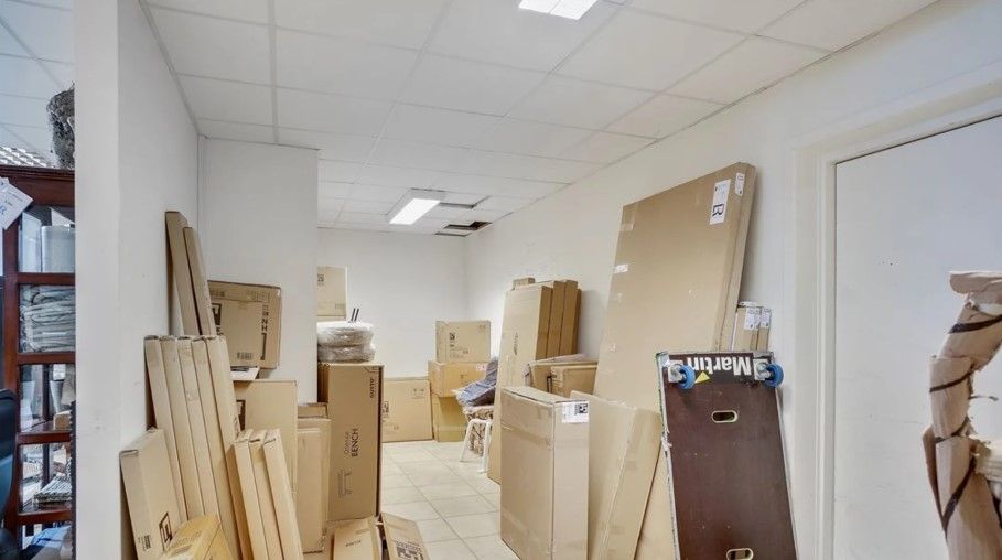 Lager med flere kartoner og trækasser. Store kartoner står opstillet mod væggen. Lyserød og blå skilt er skråt på en kasse.