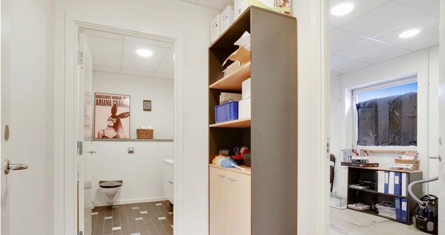 En stor indgangsdør med håndtag og et toilet i en hvid og brun farvetone. Højre side har et højt skab og et skrivebord med