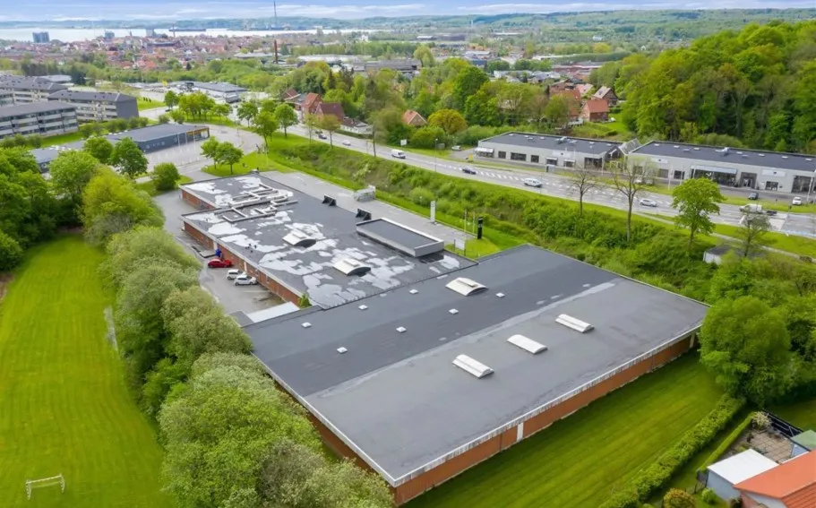 Lejemål på Løgumklostervej 138 i Aabenraa, med hele 427 kvadratmeter, omgivet af grønne træer og parkeringsplads.