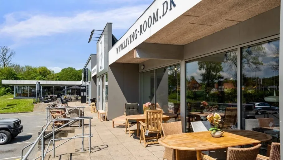 En stor terrasse med stole og borde, hvor der er et bord med en vase med blomster, sammen med en bil parkeret udenfor