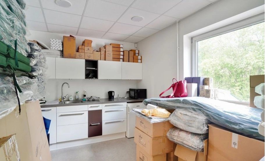 Rum med tøj, tøjstativet, køkken, køkkenbord, mikrobølgeovn, kogeplade, vandhaner, vinduesglas og papkasser placeret rundt i