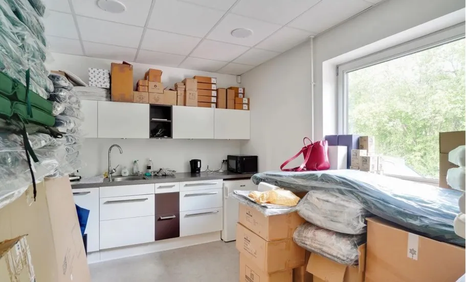 Rum med tøj, tøjstativet, køkken, køkkenbord, mikrobølgeovn, kogeplade, vandhaner, vinduesglas og papkasser placeret rundt i