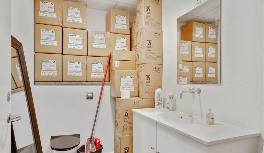 En lille lukket toiletrum med toilet, opvask og skabe med lagerkasser