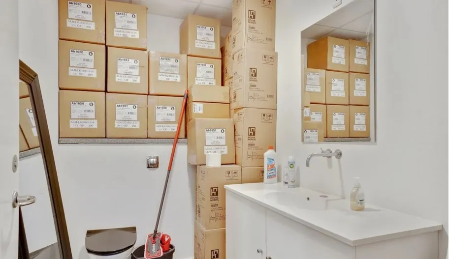 En lille lukket toiletrum med toilet, opvask og skabe med lagerkasser