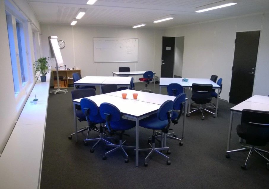 Kontorlokaler med lyse loftslampe, skriveborde, lyseblå stole og et whiteboard bagved