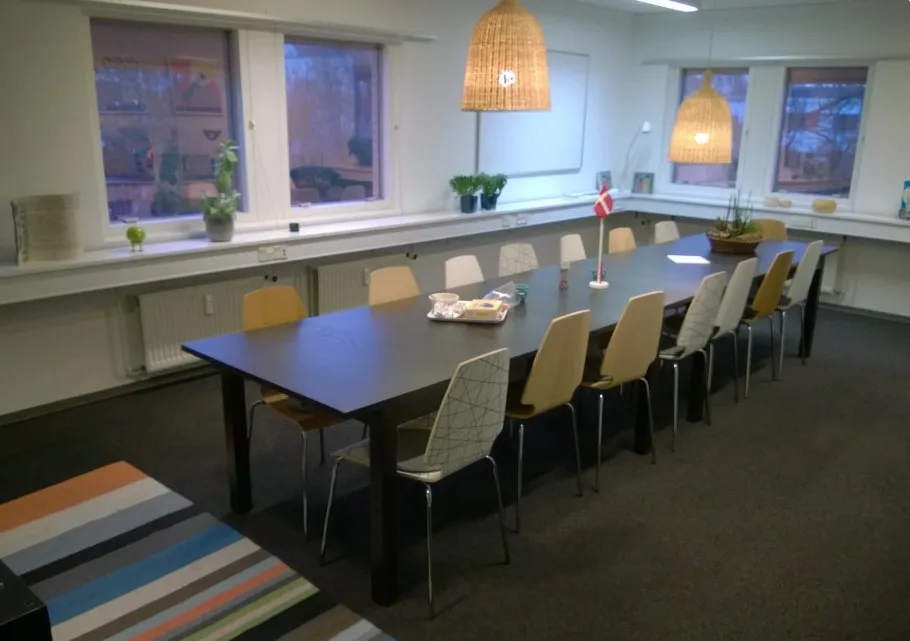 Kontorlokaler med et langt bord og stole samt lysekroner, plante og tekstur på gulvet