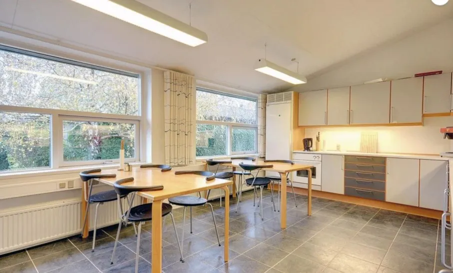 Et moderne kontor med fire borde, hver med fire stole, og en stor køkkendel med apparater