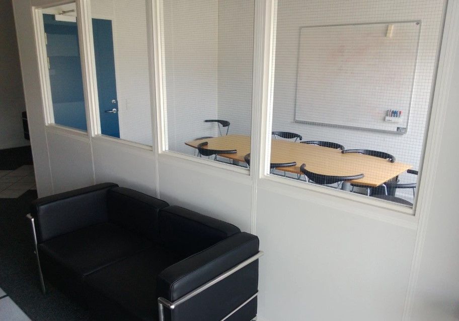 Kontorrum med bord og stole samt mødelokale med tavle og stolpe. Sort lædersofa står på gulvet.