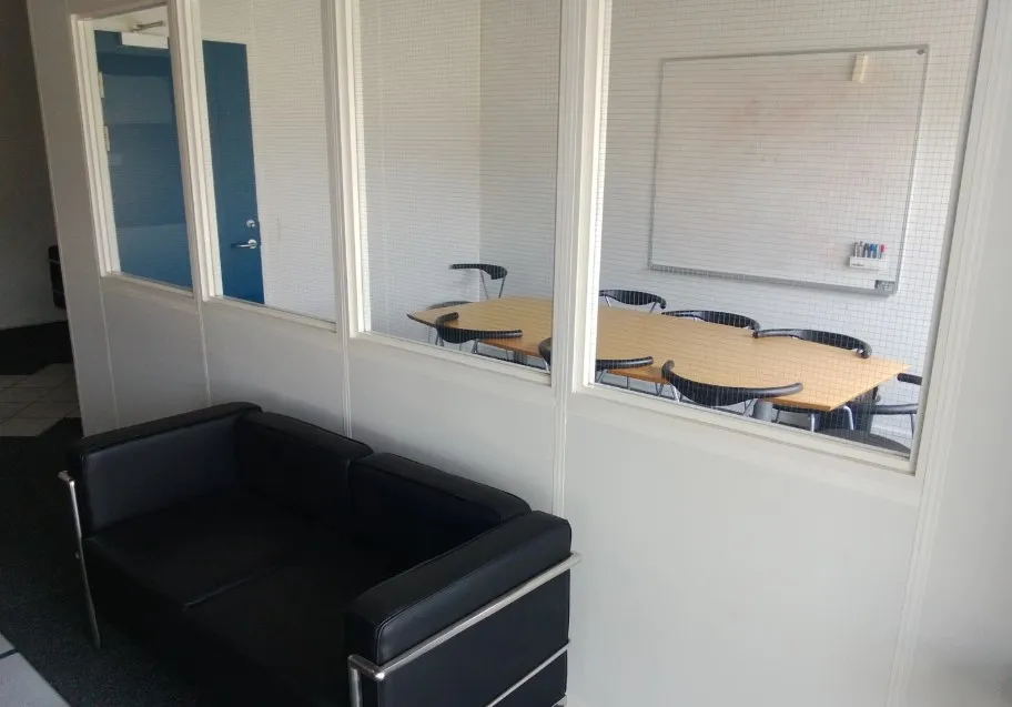 Kontorrum med bord og stole samt mødelokale med tavle og stolpe. Sort lædersofa står på gulvet.