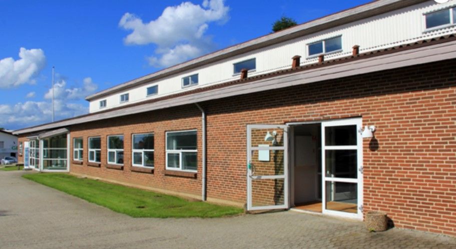 Stort kontor med lyse ruder og store glasdøre, terrasse og grønne enge foran, samt en hvidt malet skorsten