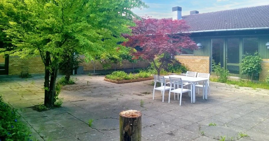 Have med bord og stole udenfor et hus med terrasse og glasvinduer