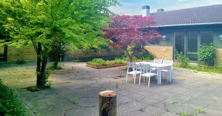 Have med bord og stole udenfor et hus med terrasse og glasvinduer