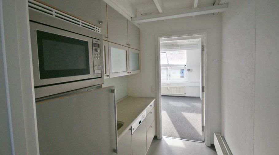 Et moderne køkken med hvide vægge, en hvid mikroovn, en køleskab og lysegrå gulvbelægning