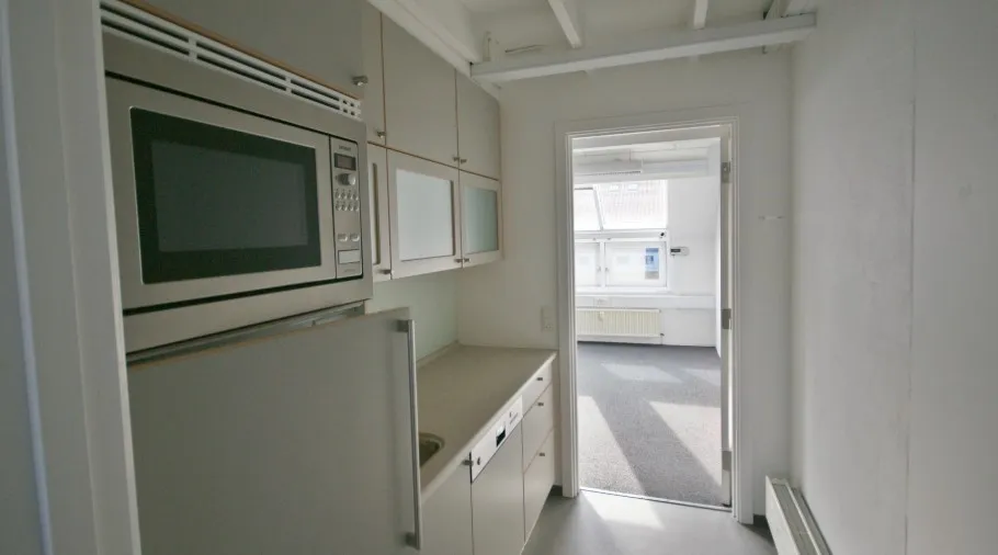 Et moderne køkken med hvide vægge, en hvid mikroovn, en køleskab og lysegrå gulvbelægning