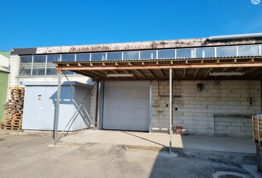 Rummeligt erhvervslokale med garage og åbent værksted. To hvide garageporte og skrånende tag.