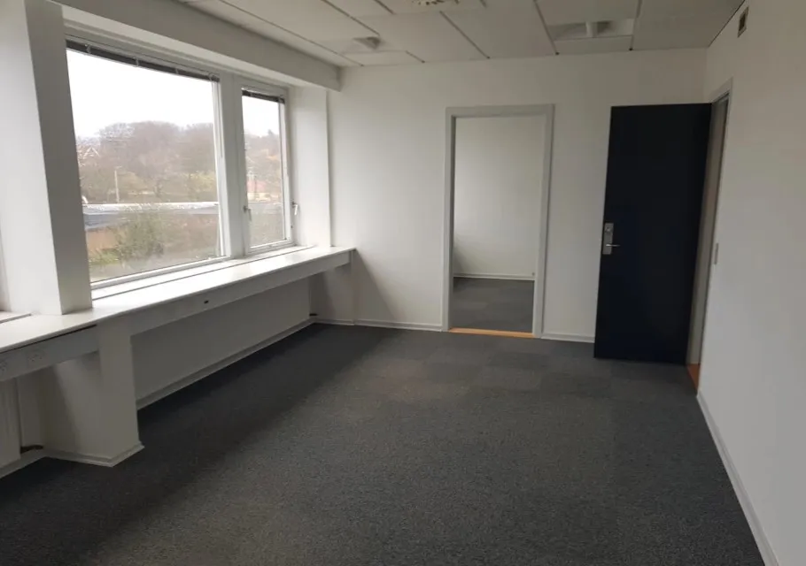 En stor, tom kontorrum med hvide vægge, gulv og loft samt en vinduesbank og en trægulv.