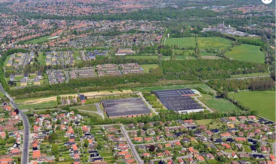 To store lagerhaller med almindelig og rampeport, omgivet af grønne marker, boliger og en bred vej