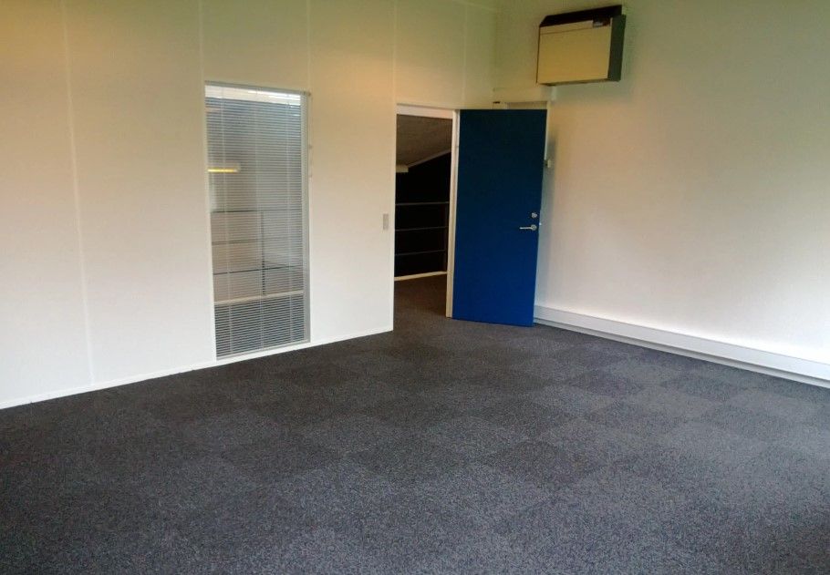 Kontor med hvid væg og gulv. Der er en glasdør med gardiner og en blå dør med håndtag. Der er et højt loft med en ventil i
