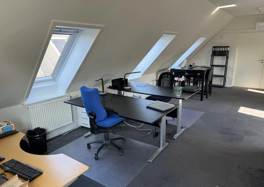 En tom kontor med to skriveborde, en høj og lav. Der er en stol og to skraldespande.