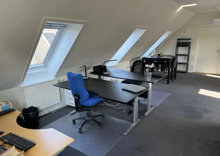 En tom kontor med to skriveborde, en høj og lav. Der er en stol og to skraldespande.