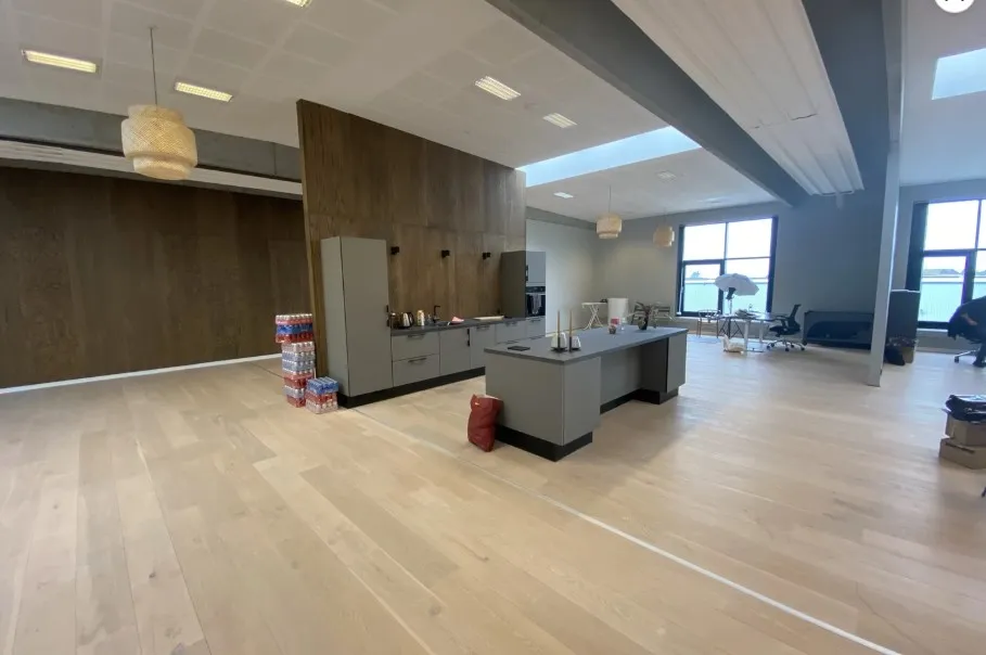 Lyst og moderne kontor med højt til loftet, masser af vinduer og lyse loftslampe. På gulvet ligger en række kartoner.