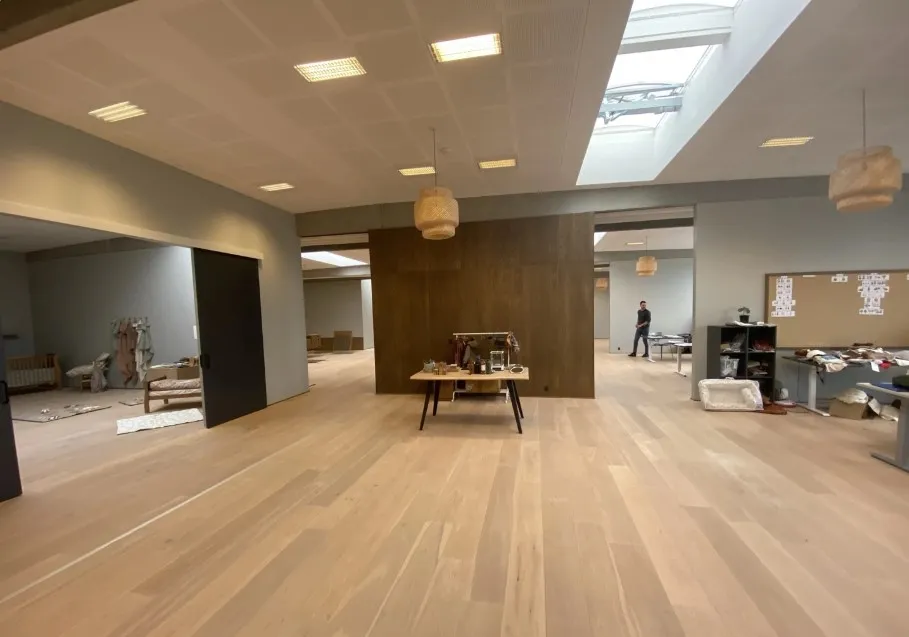 Et tomt kontor med lysegult trægulv og åbne døre og vinduer samt en enkelt person i baggrunden