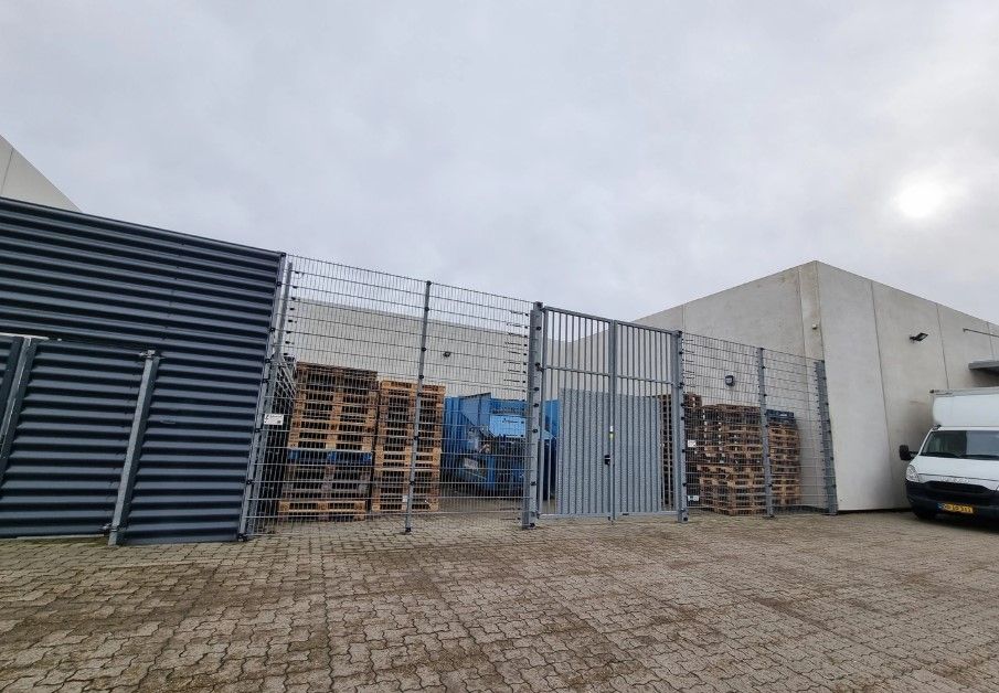 En industribygning med en stor lagerplads med stakketøj og en lastbil parkeret foran bygningen