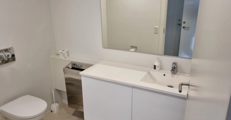 Moderne, rent og veludstyret badeværelse med hvid toilet, ren vask, spejl, håndsæbe og toiletpapir.