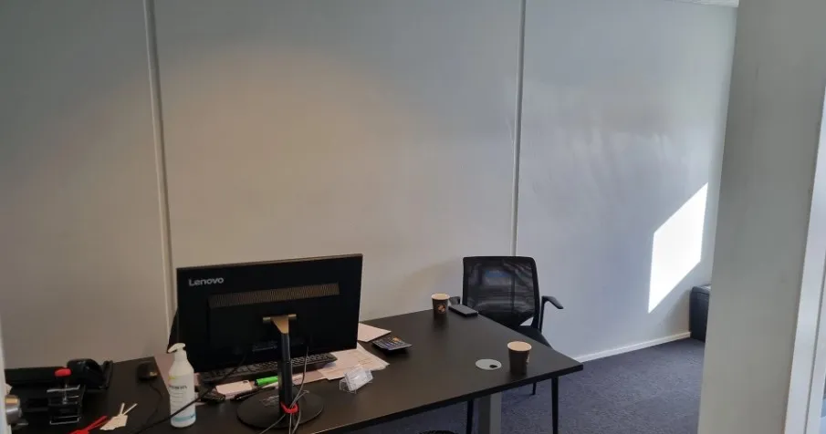 Lejlighed med kontorbord, monitor, stol, to kopper og en hvid sprayflaske på bordet