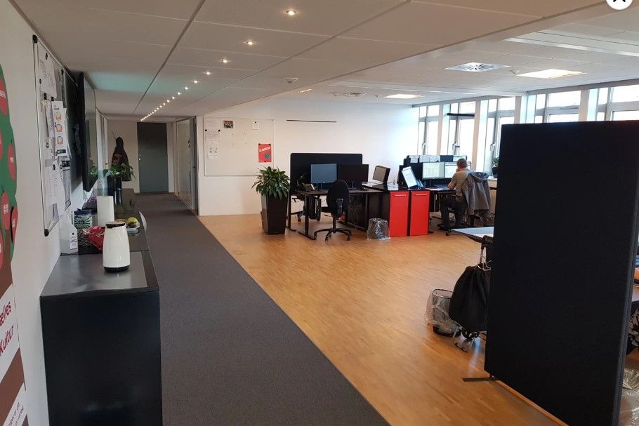 Kontor med moderne møbler og computere, hvor en person sidder og arbejder. Væggene er dekoreret med plakater og papirark.