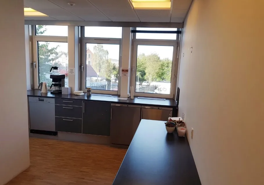 Moderne kontor med lyse vinduer, trægulv og lys plade. Kaffemaskine og køkkenredskaber på kontorbord. Faciliteter inkluderer