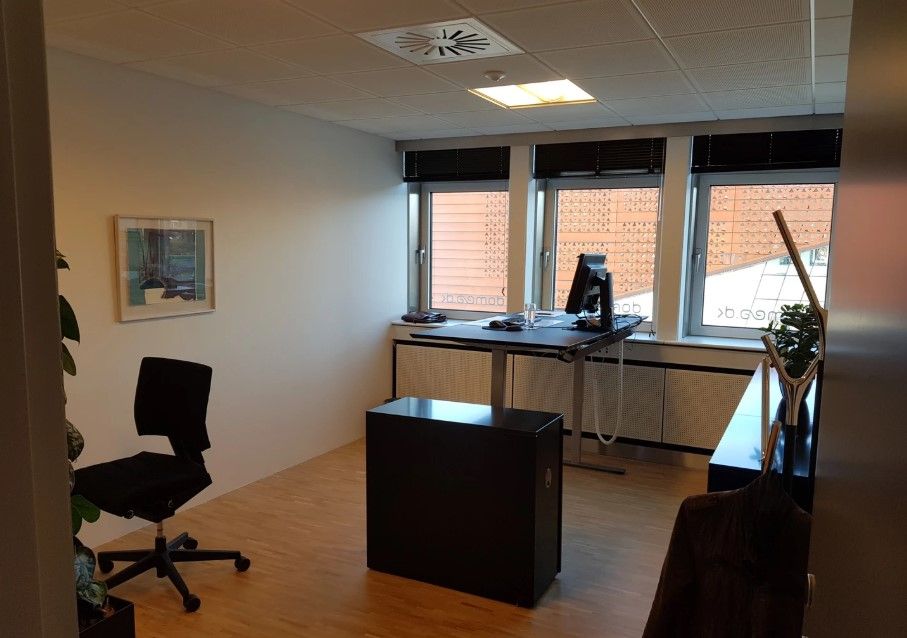 Et moderne kontor med en sort skrivebord, en computer og et sort stol samt en plante og et maleri på væggen